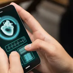 Dłoń trzyma smartfon z aplikacją zdrowie, wyświetlającą obraz serca i tętno 67.