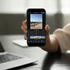 Dłoń trzyma smartfon z aplikacją do montowania filmów. Na ekranie widać oś czasu z klipami wideo i opcjami edycji.