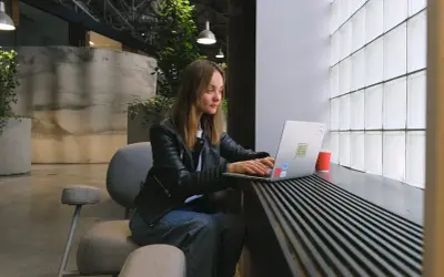 Kobieta siedzi przy laptopie, ucząc się, jak założyć konto na OLX. W tle nowoczesne wnętrze z roślinami.