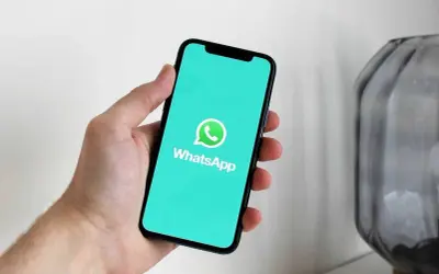 Dłoń trzyma smartfon z logo WhatsApp. Dowiedz się, jak usunąć grupę na WhatsApp, aby uporządkować swoje czaty.