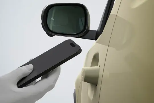 Dłoń w białej rękawiczce zbliża smartfon do klamki samochodu Hyundai. Bluelink umożliwia bezkluczykowe otwieranie.