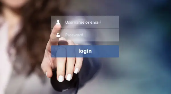 Dłoń naciska przycisk logowania. Widoczne pola na username i hasło, sugerujące proces uwierzytelniania.