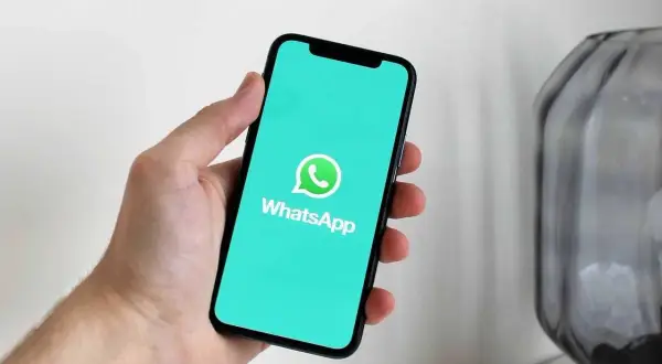 Dłoń trzyma smartfon z logo WhatsApp. Dowiedz się, jak usunąć grupę na WhatsApp, aby uporządkować swoje czaty.