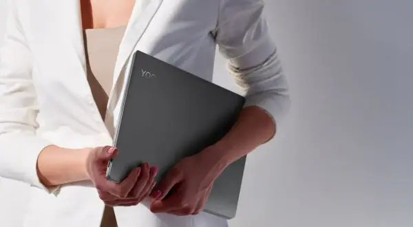 Kobieta w białej marynarce trzyma laptopa Lenovo Yoga. Czas na aktualizację systemu, by praca była płynna.