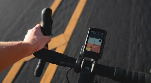 Rowerzysta trzyma kierownicę, na której zamontowana jest aplikacja na rower z mapą i danymi o trasie.