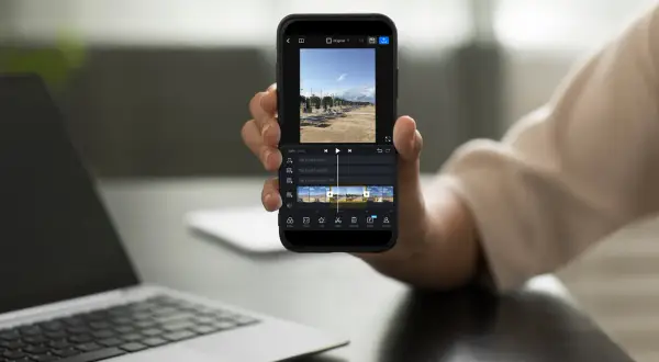 Dłoń trzyma smartfon z aplikacją do montowania filmów. Na ekranie widać oś czasu z klipami wideo i opcjami edycji.
