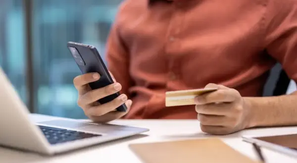 Mężczyzna trzyma telefon i kartę, szukając informacji, jak anulować subskrypcję.