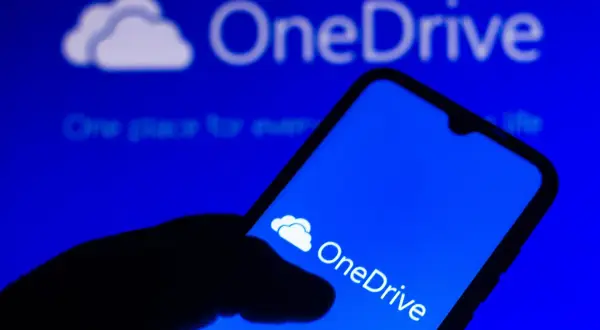Dłoń trzyma smartfon z ikoną OneDrive. Szybki OneDrive download ułatwia dostęp do plików.