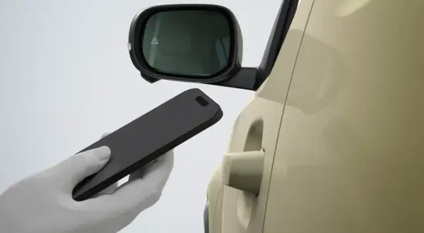 Dłoń w białej rękawiczce zbliża smartfon do klamki samochodu Hyundai. Bluelink umożliwia bezkluczykowe otwieranie.