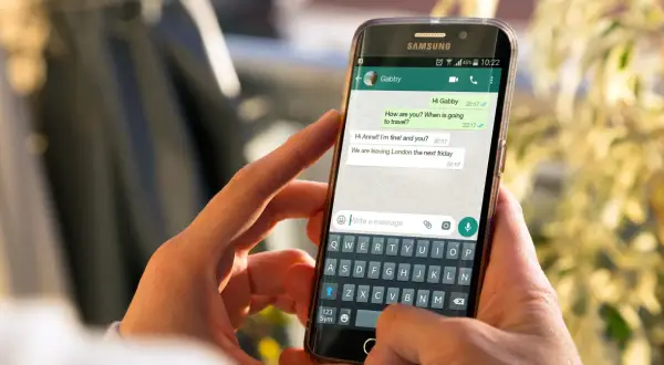 Dłonie trzymają smartfon z otwartym WhatsAppem. Widoczna jest rozmowa i klawiatura, co może pomóc w nauce jak zainstalować WhatsApp.