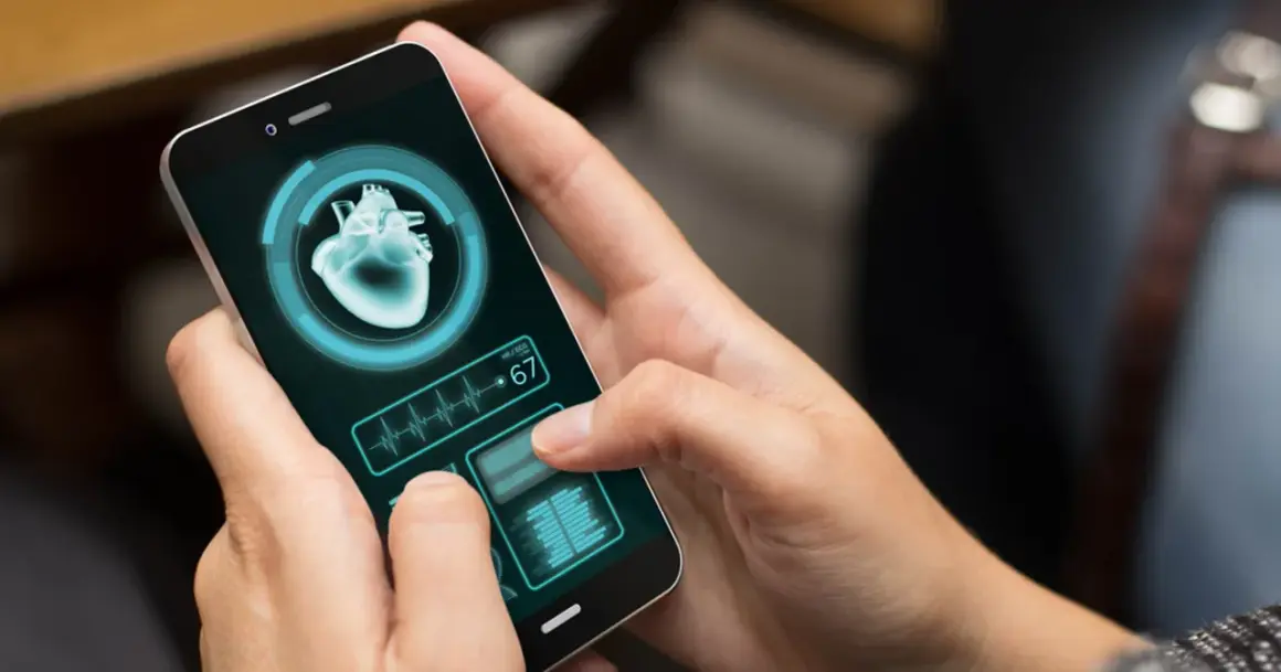 Dłoń trzyma smartfon z aplikacją zdrowie, wyświetlającą obraz serca i tętno 67.