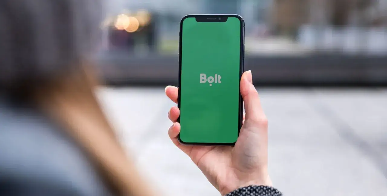 Dłoń trzyma smartfon z zielonym ekranem i logo Bolt. Szybko zamów taksówkę!